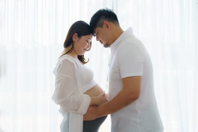 A pregnant couple standing in front of a window.